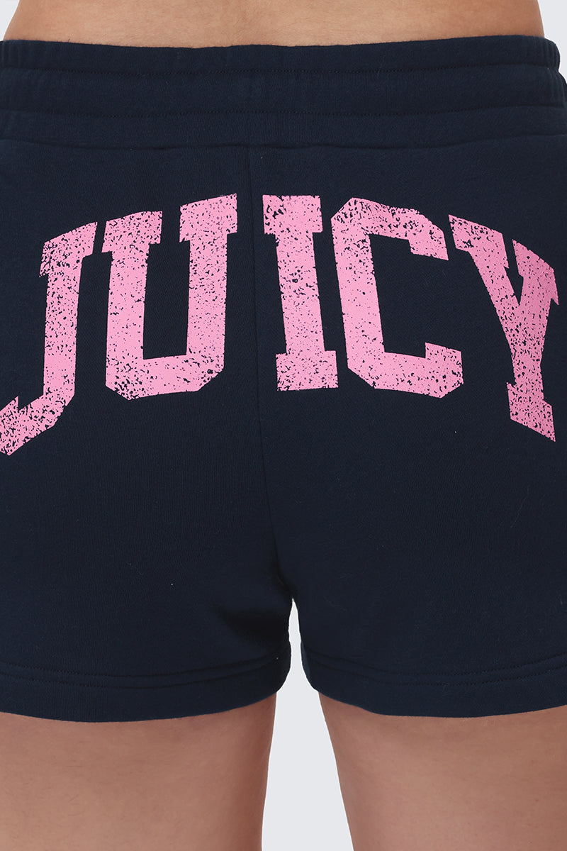 A close-up of the back of Collegiate Booty Shorts, dark terry with a drawstring waist and “JUICY” in large, distressed pink letters across the fabric.