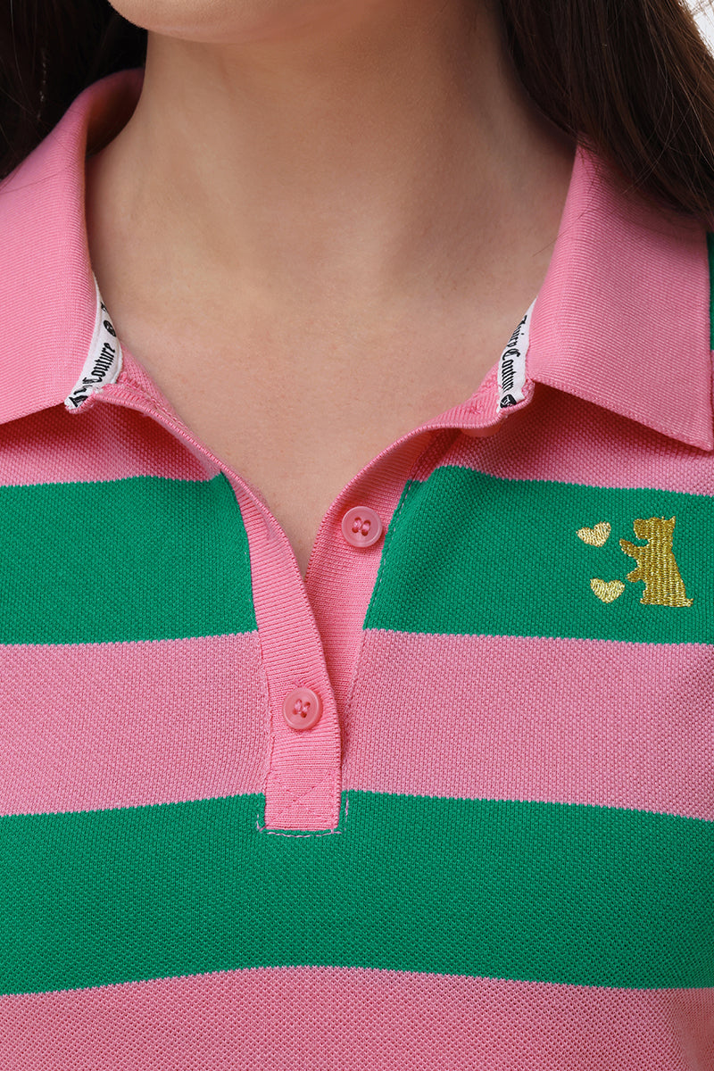 A close-up of a person wearing the Stripe Embroidered Baby Polo, featuring bold pink and green stripes, an embroidered gold dog with hearts on the left chest, and a collar lined in white with black text.