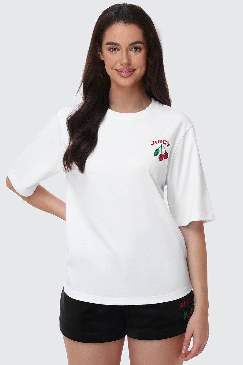 A woman with long dark hair wears the Cherry Bling Graphic Tee featuring a cherry graphic and JUICY text, paired with black shorts with a rhinestone Juicy cherry. She smiles against a plain background.