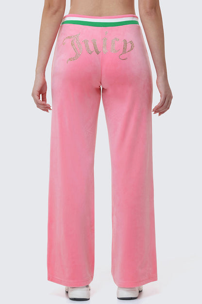 Wearing Heritage Stripe Bling Velour Track Pants, which feature pink velour, a Juicy rhinestone logo on the back, and a green and white striped waistband, the person stands against a light gray background.
