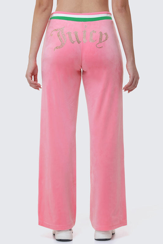Wearing Heritage Stripe Bling Velour Track Pants, which feature pink velour, a Juicy rhinestone logo on the back, and a green and white striped waistband, the person stands against a light gray background.