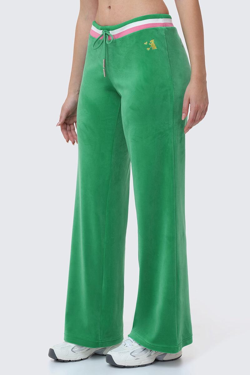 Someone wears Heritage Stripe Bling Velour Track Pants in bright green with a sporty striped waistband, drawstring, small embroidered yellow logo on the left hip, paired with white sneakers.