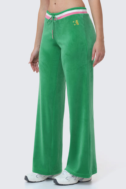 Someone wears Heritage Stripe Bling Velour Track Pants in bright green with a sporty striped waistband, drawstring, small embroidered yellow logo on the left hip, paired with white sneakers.