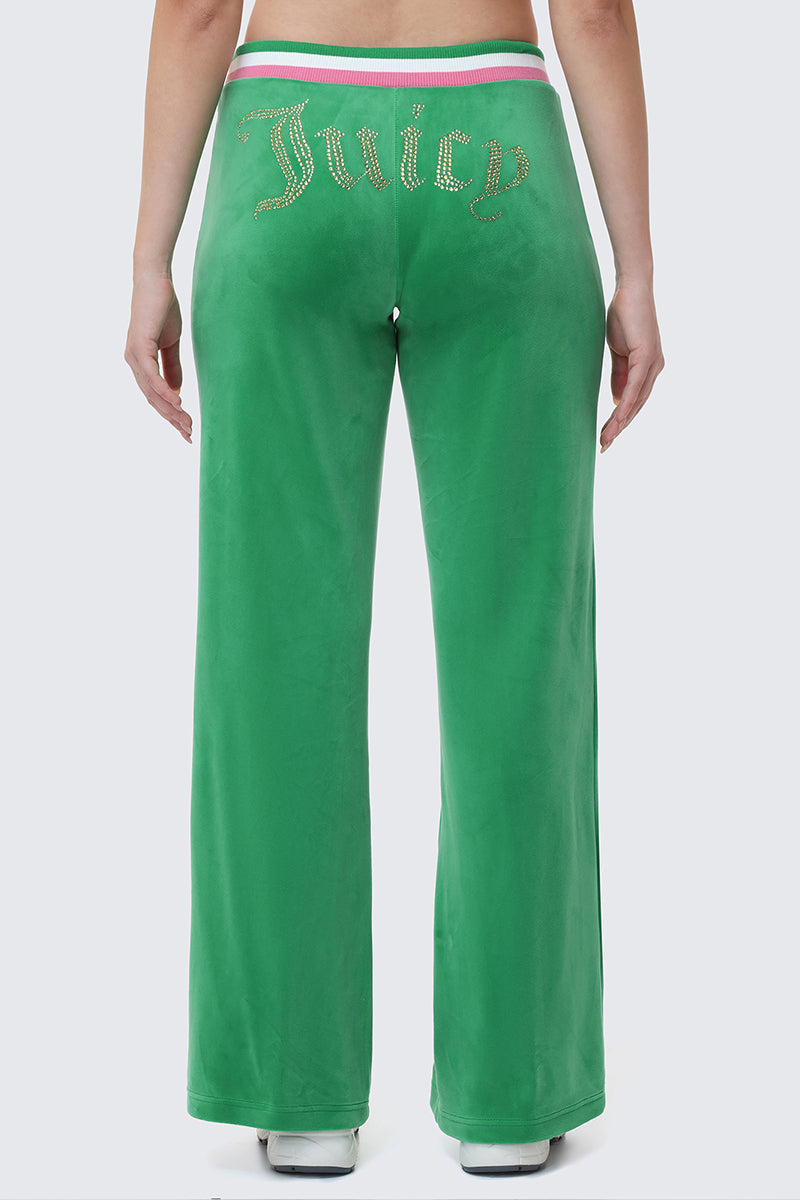 Someone stands with their back to the camera, wearing Heritage Stripe Bling Velour Track Pants featuring a rhinestone Juicy logo on the back and a sporty striped waistband.