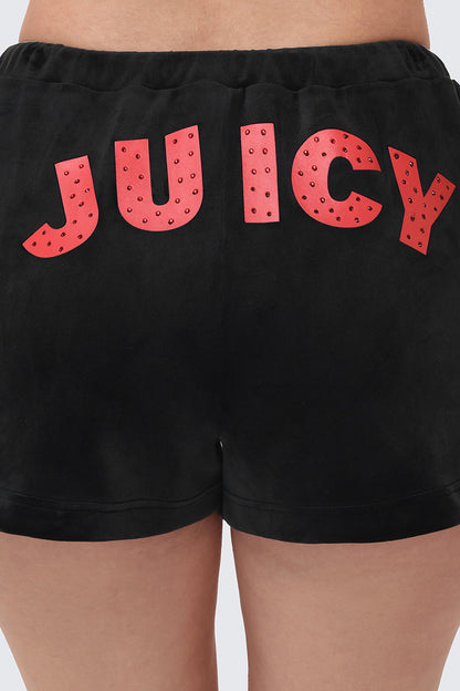 A close-up of a person wearing Cherry Bling Velour Shorts, featuring the word JUICY in bold red letters with small stud accents across the back.