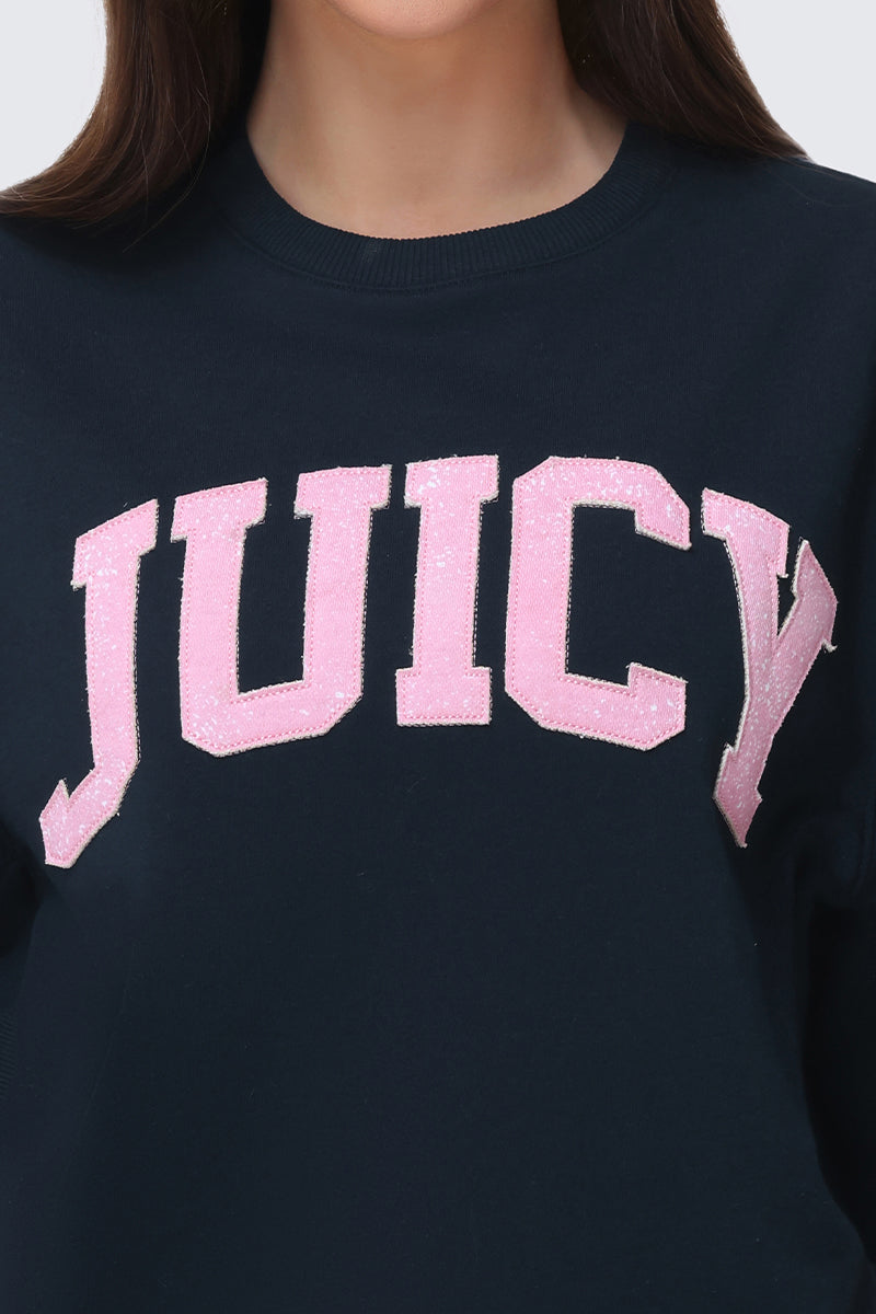 Someone wearing the Collegiate Sweatshirt, a dark Juicy design featuring large, glittery pink "JUICY" lettering on the front. Only the lower half of the face and upper torso are shown.