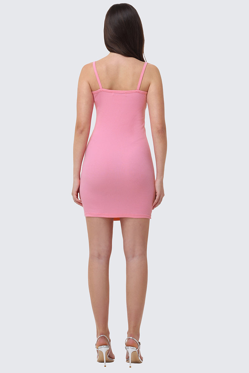 A woman faces away, wearing the pink Big Bling Mini Dress with a rhinestone Juicy logo and white high-heeled sandals. Her straight brown hair is down, set against a light gray background.