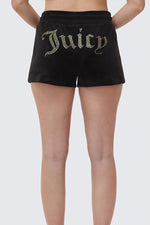 Someone stands with hands on hips, facing away to show off black Big Bling Velour Shorts featuring a large gold rhinestone Juicy logo across the back.
