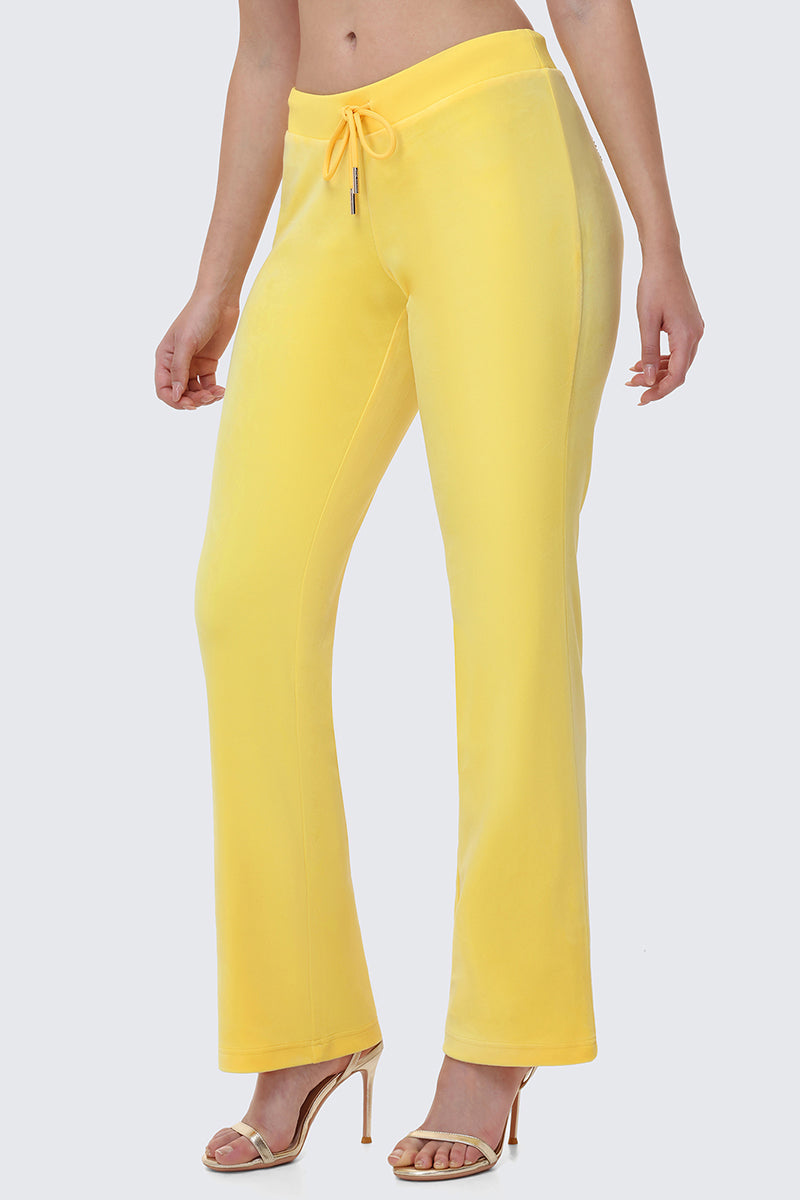 Someone wears OG Big Bling Velour Track Pants in bright yellow and beige high-heeled sandals, shown from waist to feet against a plain light background.