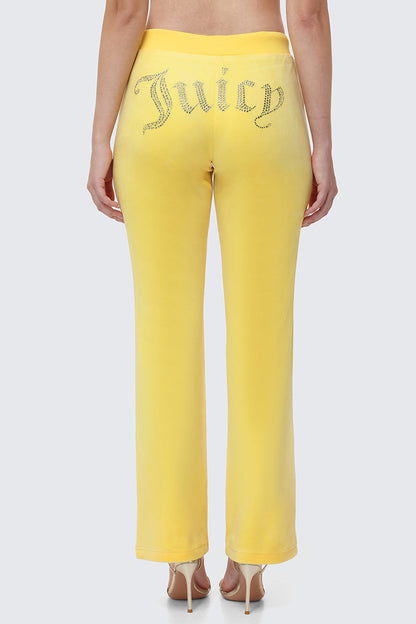 A woman shows off Y2K style in OG Big Bling Velour Track Pants with “Juicy” in rhinestones on the back, posing with her back to the camera and pairing the look with high-heeled sandals.