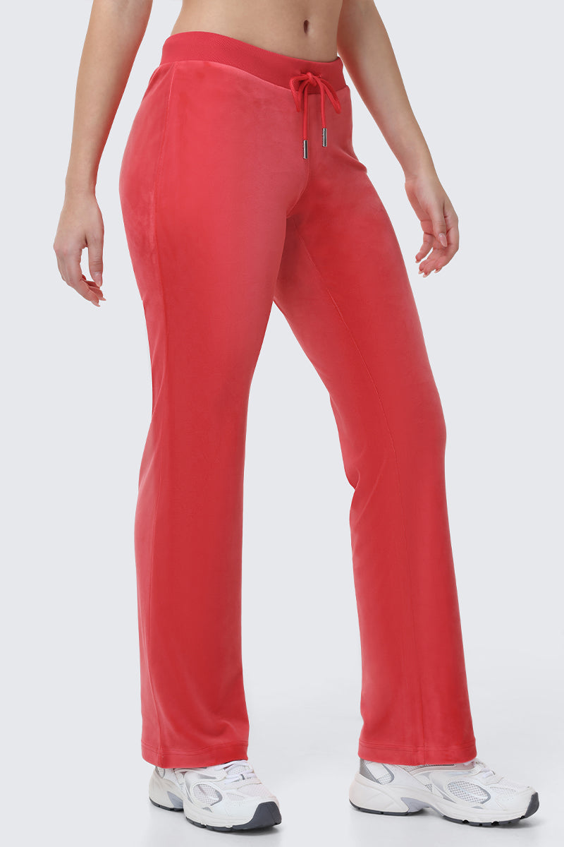 Wearing OG Big Bling Velour Track Pants in bright red, a person stands in white sneakers, the focus on their legs and waist against a plain light background.