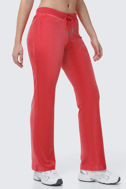 Wearing OG Big Bling Velour Track Pants in bright red, a person stands in white sneakers, the focus on their legs and waist against a plain light background.