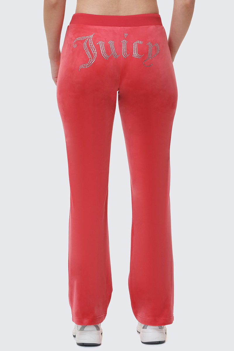 Someone wearing bright pink OG Big Bling Velour Track Pants with "Juicy" in rhinestones across the back stands facing away, highlighting the iconic look from behind.