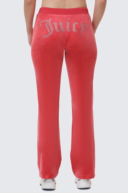Someone wearing bright pink OG Big Bling Velour Track Pants with "Juicy" in rhinestones across the back stands facing away, highlighting the iconic look from behind.