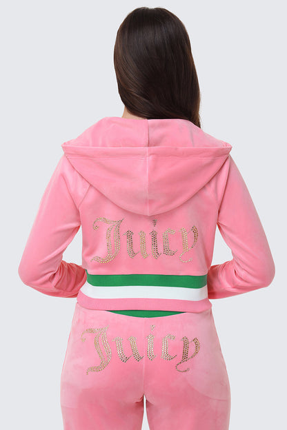 A woman with long brown hair is seen from behind wearing the Juicy Couture Heritage Stripe Bling Velour Zip Hoodie in pink, featuring a rhinestone logo on the back, a hood, and a green and white striped waistband.