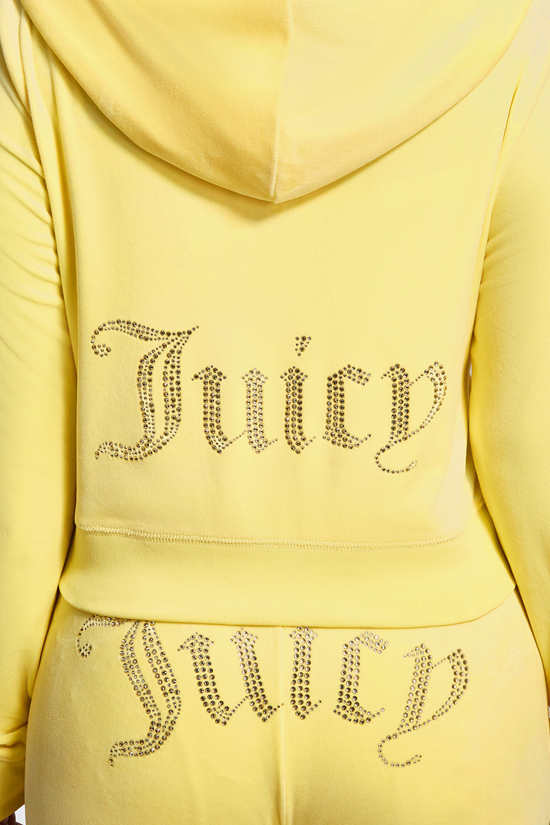 A close-up of a person in the Plus-Size OG Big Bling Velour Hoodie, featuring yellow velour fabric and “Juicy” spelled out in rhinestones on the back of both the hoodie and pants for a luxe effect.