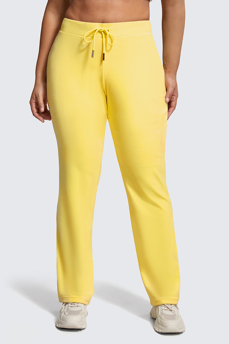 A person wearing Plus-Size OG Big Bling Velour Track Pants in bright yellow with white sneakers stands against a plain light grey background.