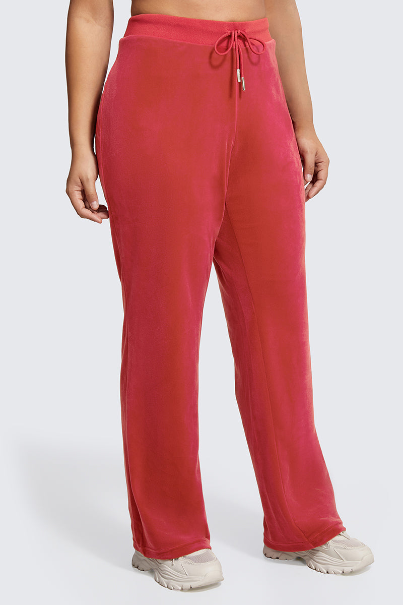 A person wears Plus-Size OG Big Bling Velour Track Pants in bright pink with white sneakers, shown from waist to feet against a light gray background.
