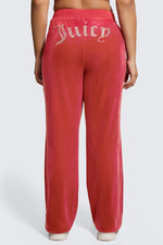 A person stands with their back to the camera against a plain light background, wearing Plus-Size OG Big Bling Velour Track Pants featuring Y2K-inspired red velour and a sparkling Juicy rhinestone embellishment on the back.