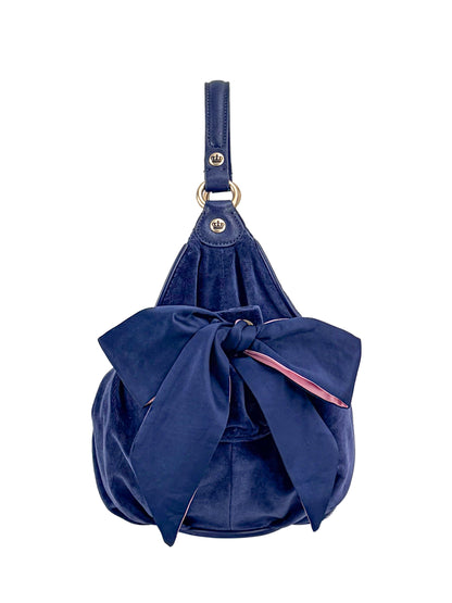 The Royal Bloom Hobo Bag is a navy blue handbag with a large matching front bow and a short handle with metal rings, showcased against a white background.