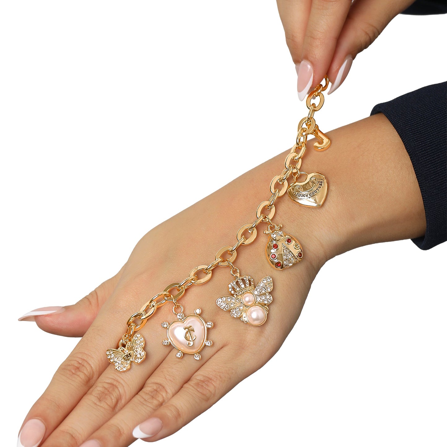 A hand with light pink manicured nails wears the Pearl & Icon Charm Bracelet, a gold-tone piece adorned with heart, bee, butterfly, and pearl-studded charms. Another hand holds its adjustable chain above the wrist.