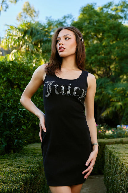 In a lush garden, a woman poses in the Big Bling Tank Dress, its sparkling "Juicy" embellishment catching the sunlight as she stands amid vibrant greenery.