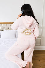 A woman kneels on a bed, talking on the phone, wearing the Plus-Size Made Me Do It Hollywood Heritage Hoodie with gold lettering in a stylish bedroom.