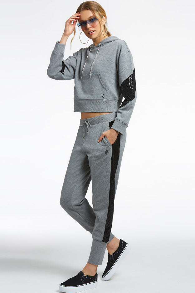 A woman in sunglasses poses in a gray hooded sweatshirt and joggers, black slip-on shoes, ideal for layering over the Crochet Maxi Dress with its colorful hem, against a white background.