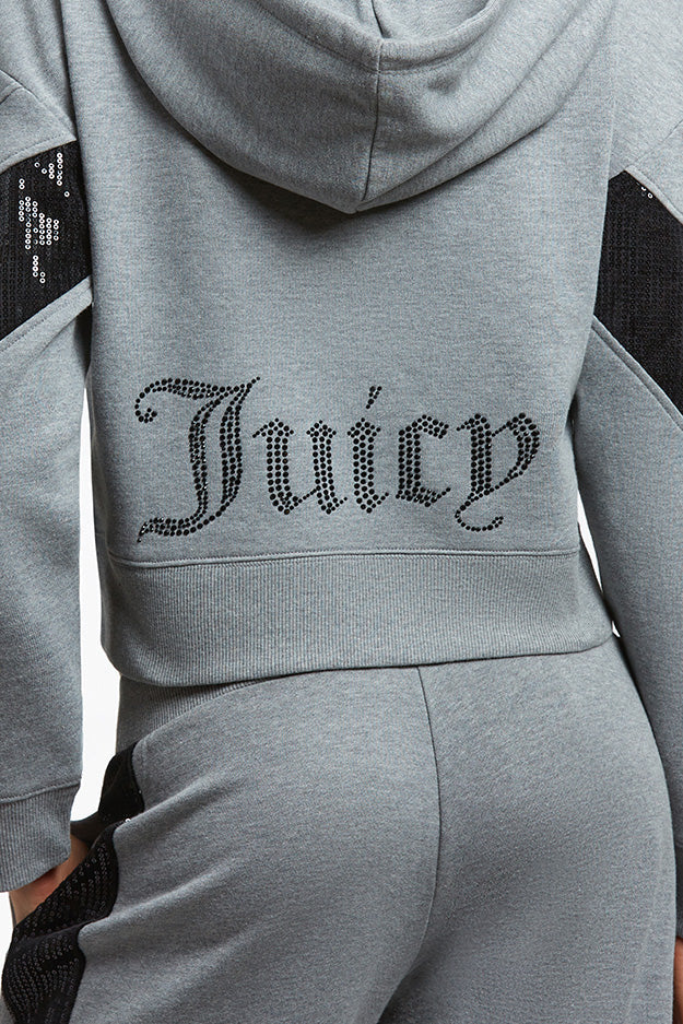 A person wears a gray velour tracksuit with "Juicy" in black rhinestones on the hoodie back, black sleeve and side details, and a hint of the Crochet Maxi Dress's colorful hem peeking out like a vacation dress.
