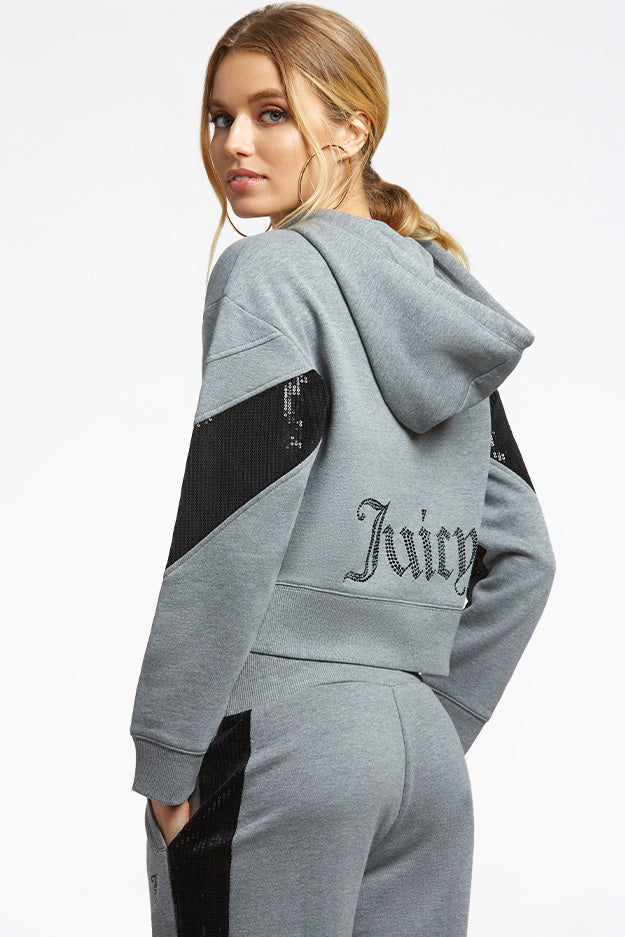 A woman in a gray hoodie and sweatpants with black sequin accents looks over her shoulder. Layer the hoodie, featuring "Juicy" in sparkly lettering on the back, over your Crochet Maxi Dress for a playful vacation look.
