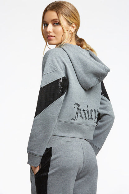 A woman in a gray hoodie and sweatpants with black sequin accents looks over her shoulder. Layer the hoodie, featuring "Juicy" in sparkly lettering on the back, over your Crochet Maxi Dress for a playful vacation look.