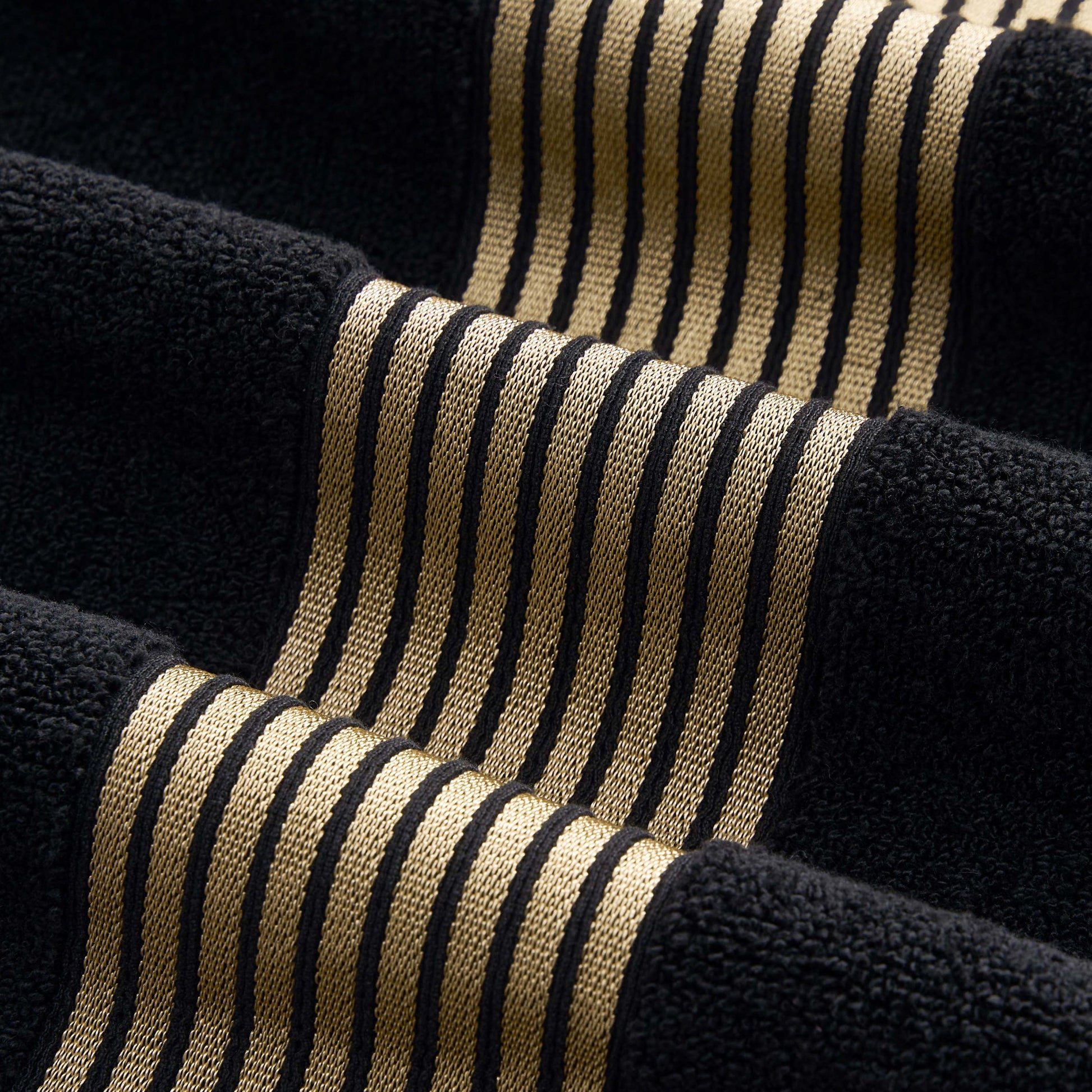 A close-up of textured fabric with black and gold stripes, showcasing raised and flat sections for a wavy 3D effect like the premium weave found in the Melissa Bath Towel Set.