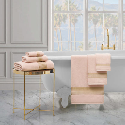 A luxurious bathroom with a freestanding white tub, gold fixtures, and a stacked Melissa Bath Towel Set on a gold side table, plus large windows revealing palm trees and mountains in the background.