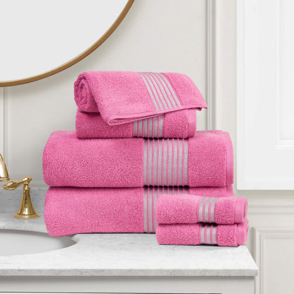 A stack of pink Melissa Bath Towel Set with gray stripes is neatly arranged on a marble bathroom counter beside a gold faucet and round mirror.
