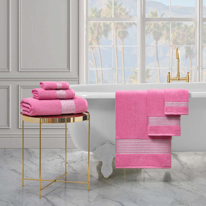 A luxurious bathroom features a white clawfoot tub, a gold side table with the Melissa Bath Towel Set, and matching pink towels hanging on the tub. Large windows offer views of palm trees outside.