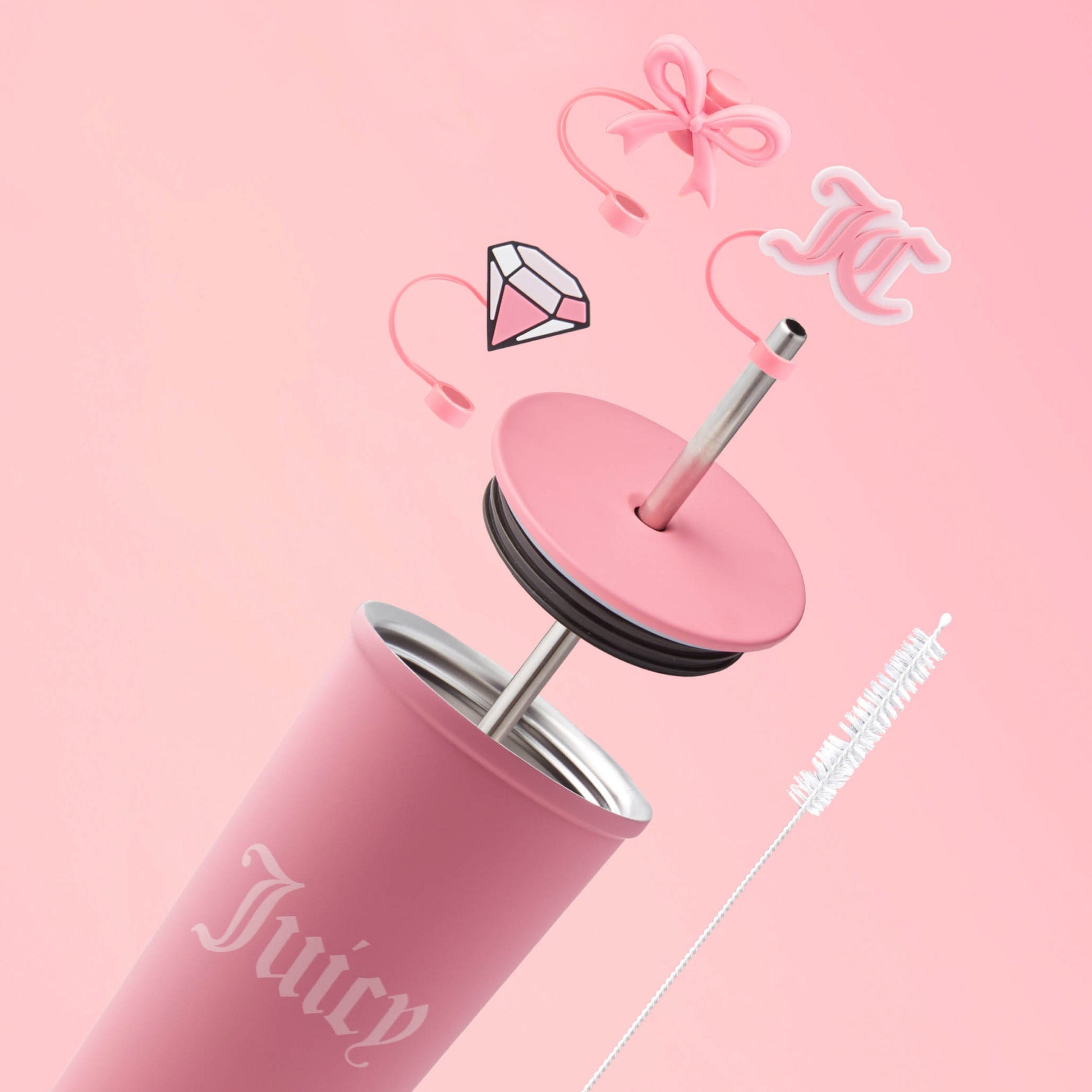 The Couture Hydration Stainless Steel Tumbler Cup 6-Piece Set features a pink Juicy Couture tumbler with lid, straw, playful floating charms (pink bow, diamond, “JC” monogram), and a white cleaning brush for a chic touch.