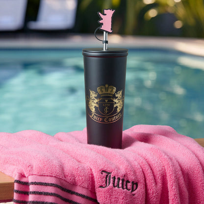 A Couture Hydration Stainless Steel Tumbler Cup from the 6-Piece Set, featuring a gold logo and pink bear topper, rests on a pink Juicy towel by the pool with palm trees and sparkling water in the background.