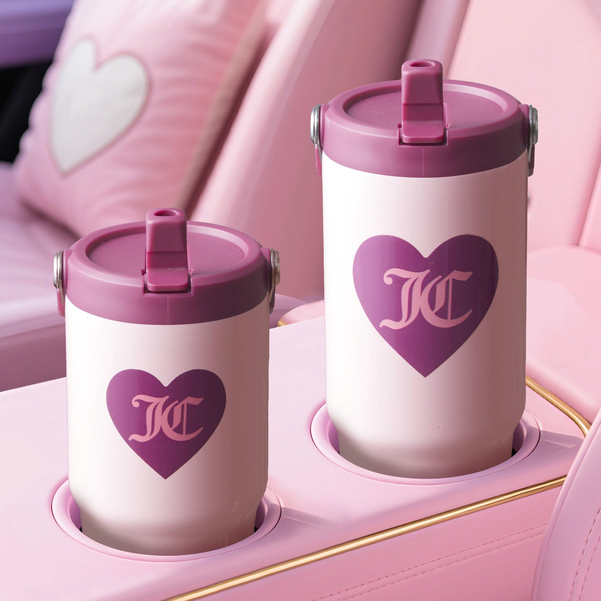Two white Flip Flow Hydration Stainless Steel Tumbler Cups with purple lids and heart designs sit in matching pink cup holders in a pastel pink car interior featuring heart-shaped seat details.