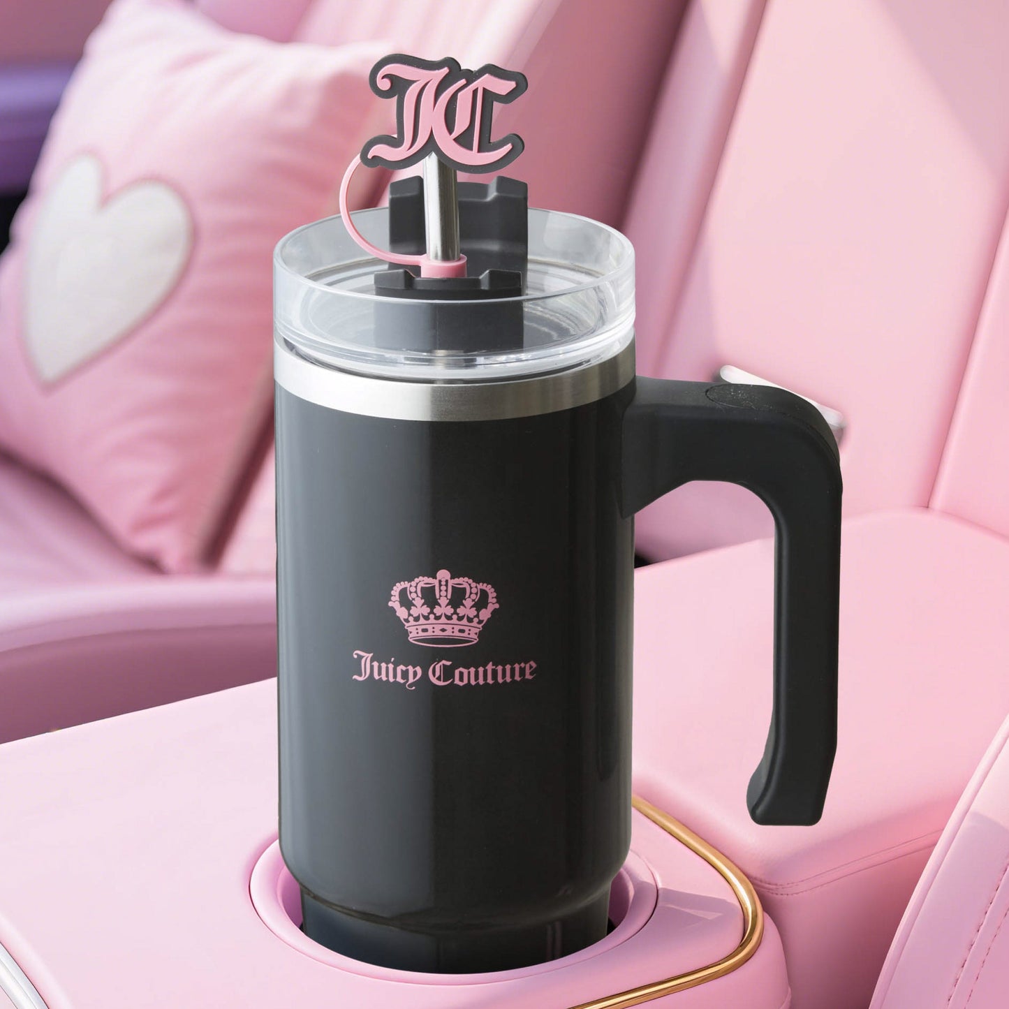 A black Jetsetter Hydration Stainless Steel Tumbler with handle sits in a pink cup holder, featuring a pink crown logo, JC straw topper, and matching the heart detail of the car, plus a neoprene crossbody pouch.