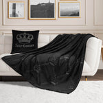 A white sofa with a black Juicy Couture pillow and the Embossed Plush Throw Blanket sits in a modern living room featuring framed art on the wall and a white rug on the floor.