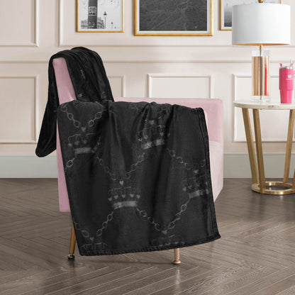 An Embossed Plush Throw Blanket with a subtle crown and chain pattern is draped over a pink velvet chair in a modern living room with light walls, framed art, a round side table, and a white lamp.