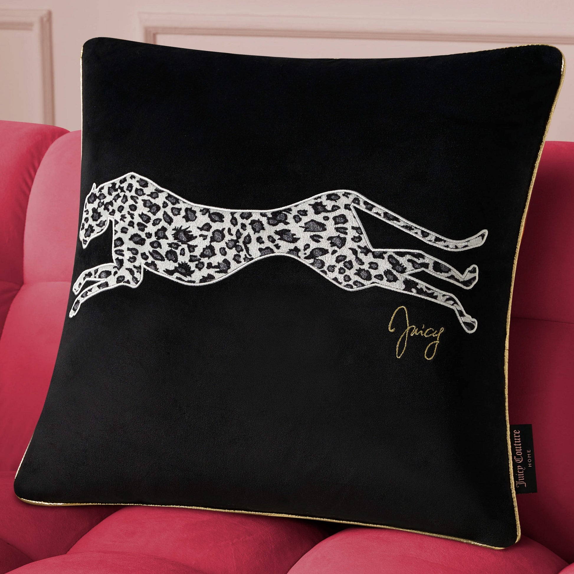 The Velvet Cheetah Square Pillow features gold piping, a white cheetah print illustration, and "Juicy" in gold script—making it a chic decorative accent for any pink sofa.