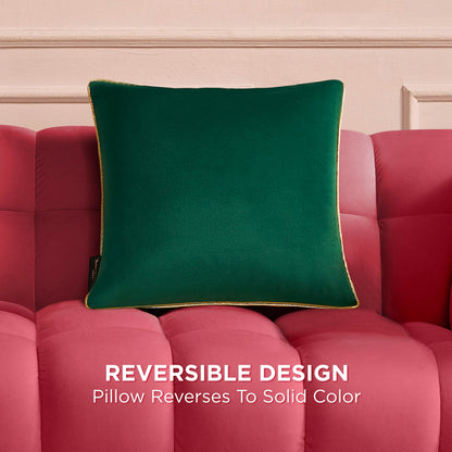 A Velvet Cheetah Square Pillow with gold piping rests on a pink tufted sofa against a light pink wall. Text reads: “REVERSIBLE DESIGN. Pillow reverses to solid color.”.