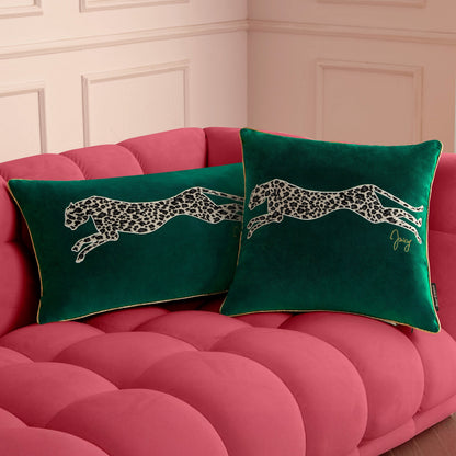 Two green Velvet Cheetah Square Pillows with bold cheetah appliques sit on a plush tufted pink sofa in front of a cream-colored wall with decorative molding.