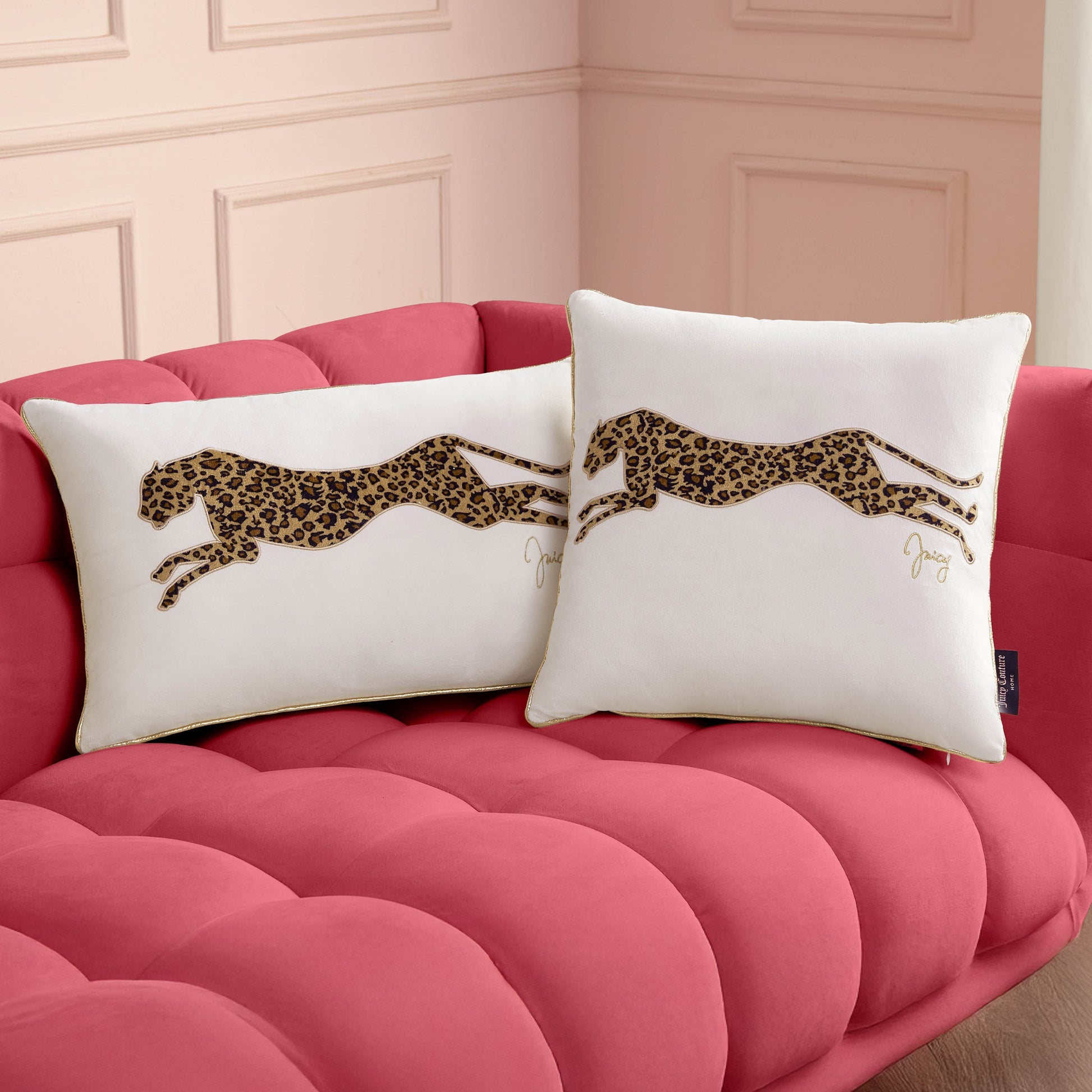 Two Velvet Cheetah Pillows with a leopard print leaping cheetah design sit on a plush pink tufted sofa against pale pink paneled walls, adding a luxe accent to this chic room.