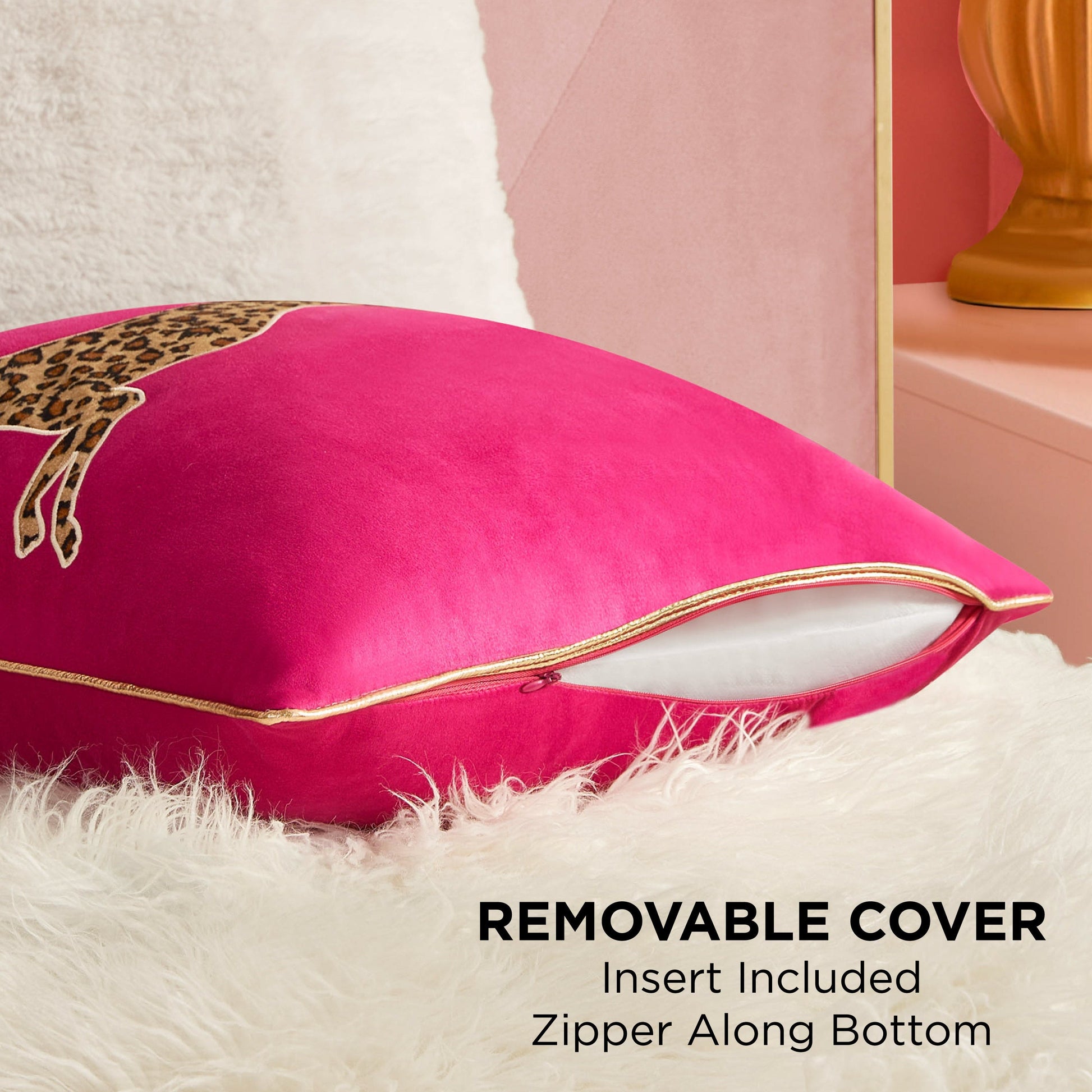 A vibrant pink Velvet Cheetah Square Pillow with gold piping and a leopard print sits on a white fur surface. Its cover is partially unzipped at the bottom, showing the insert. Text: REMOVABLE COVER, Insert Included, Zipper Along Bottom.