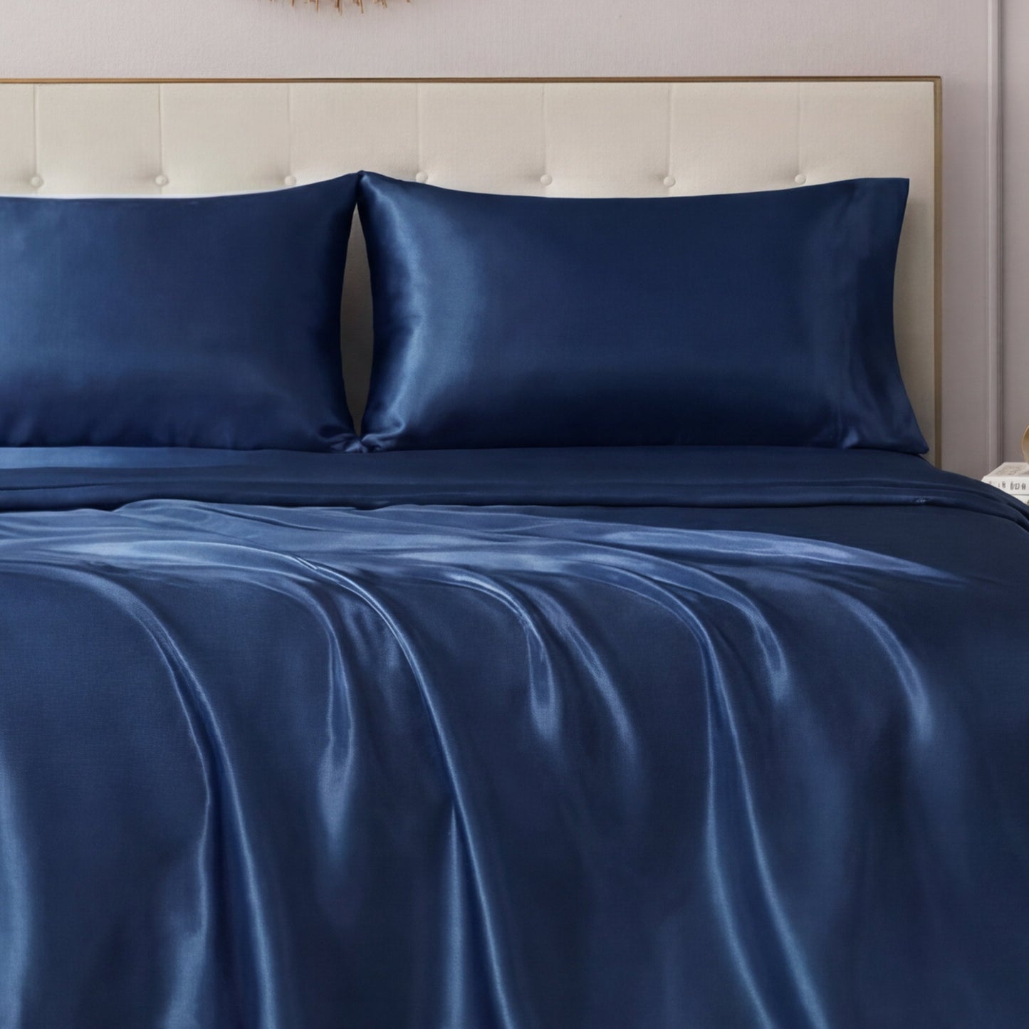 A neatly made bed features the Solid Satin Sheet Set by Juicy Couture with ultra-soft, glossy sheets and matching pillowcases, all set against a light-colored tufted headboard.