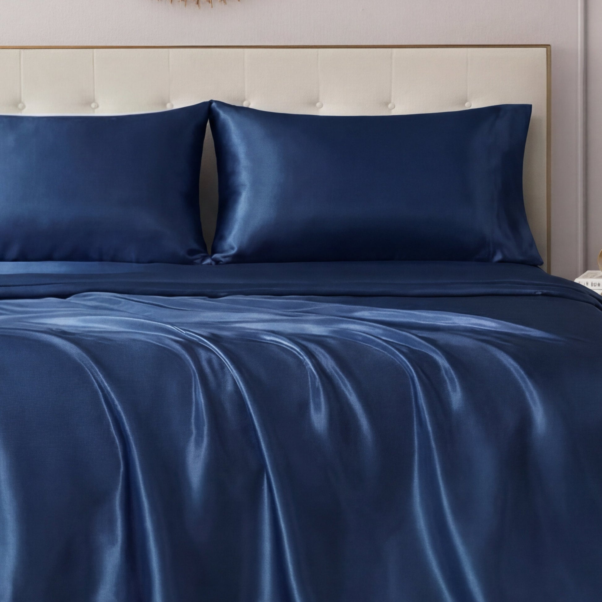 A neatly made bed features the Solid Satin Sheet Set by Juicy Couture with ultra-soft, glossy sheets and matching pillowcases, all set against a light-colored tufted headboard.