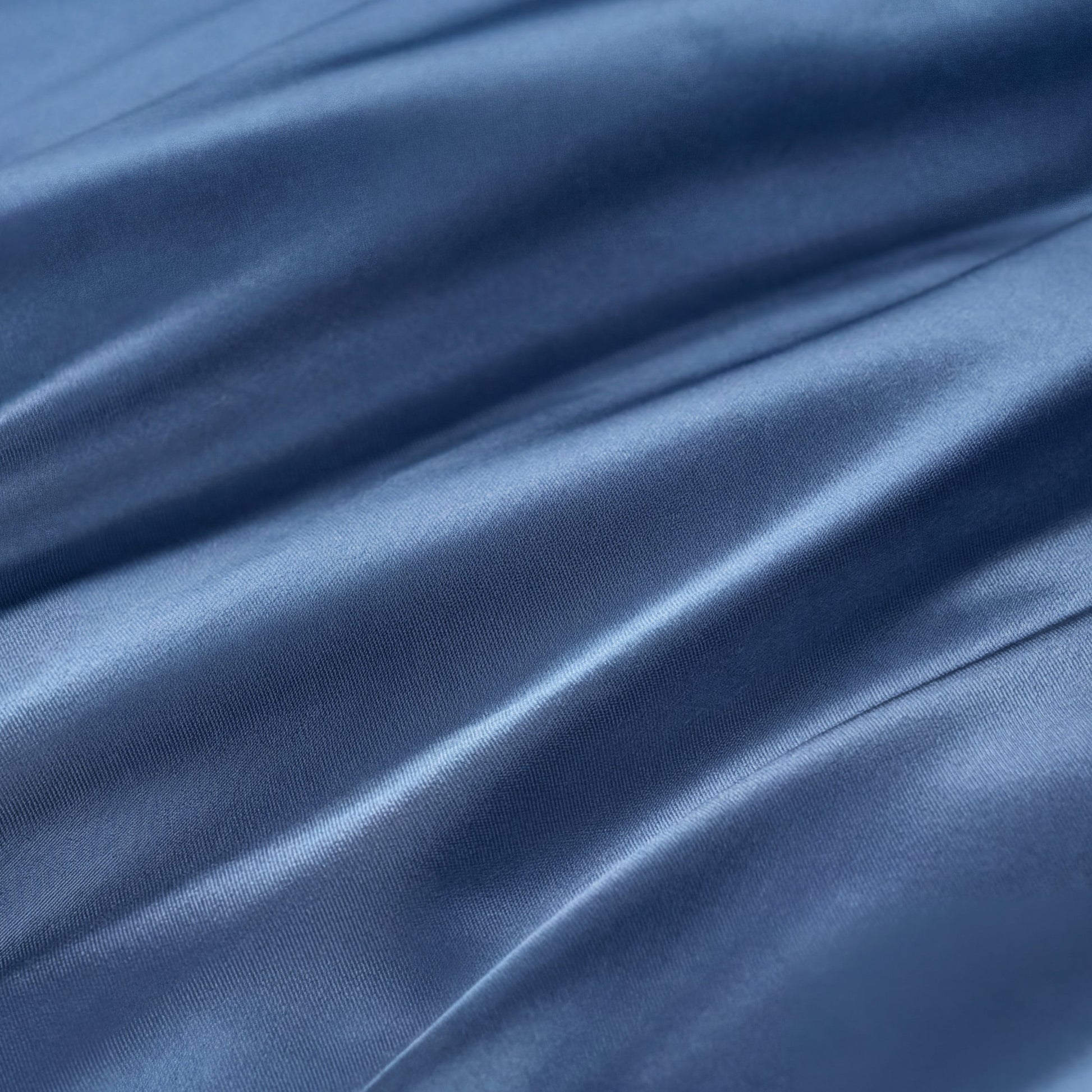 Close-up of smooth, shiny blue fabric with soft folds and gentle shadows, highlighting its silky texture—perfect for the ultra-soft Solid Satin Sheet Set.