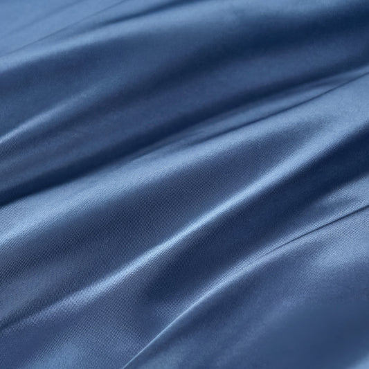Close-up of smooth, shiny blue fabric with soft folds and gentle shadows, highlighting its silky texture—perfect for the ultra-soft Solid Satin Sheet Set.